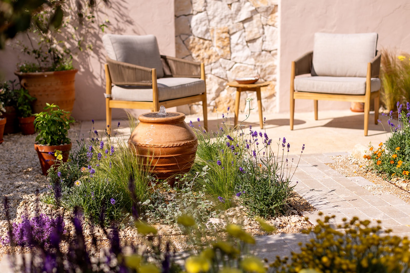 A sunny garden scene featuring potted plants, colorful flowers, and a stone pathway leading to a quaint building.
