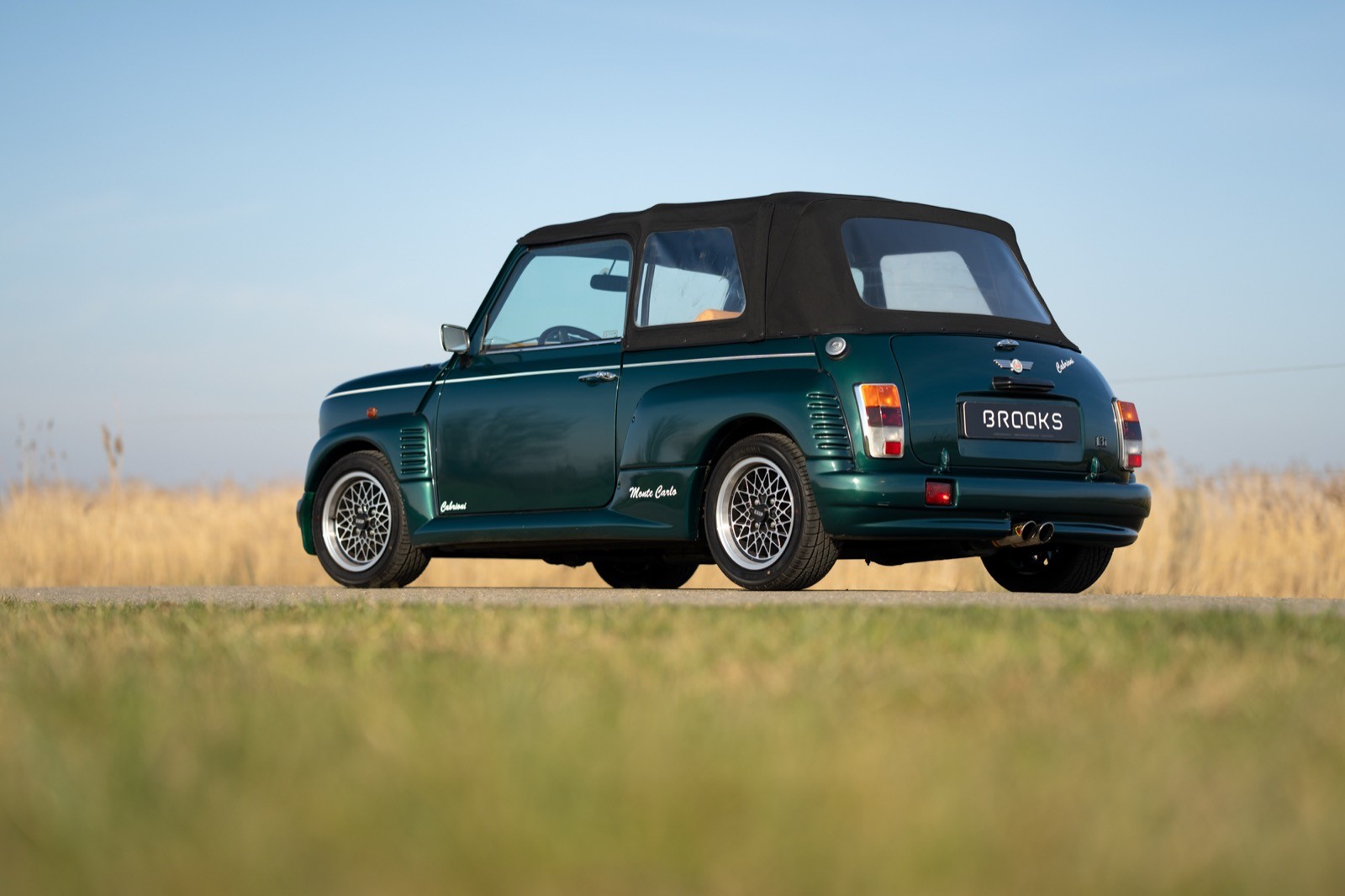 A vintage green car with a black soft top parked on grassy terrain under a clear blue sky.