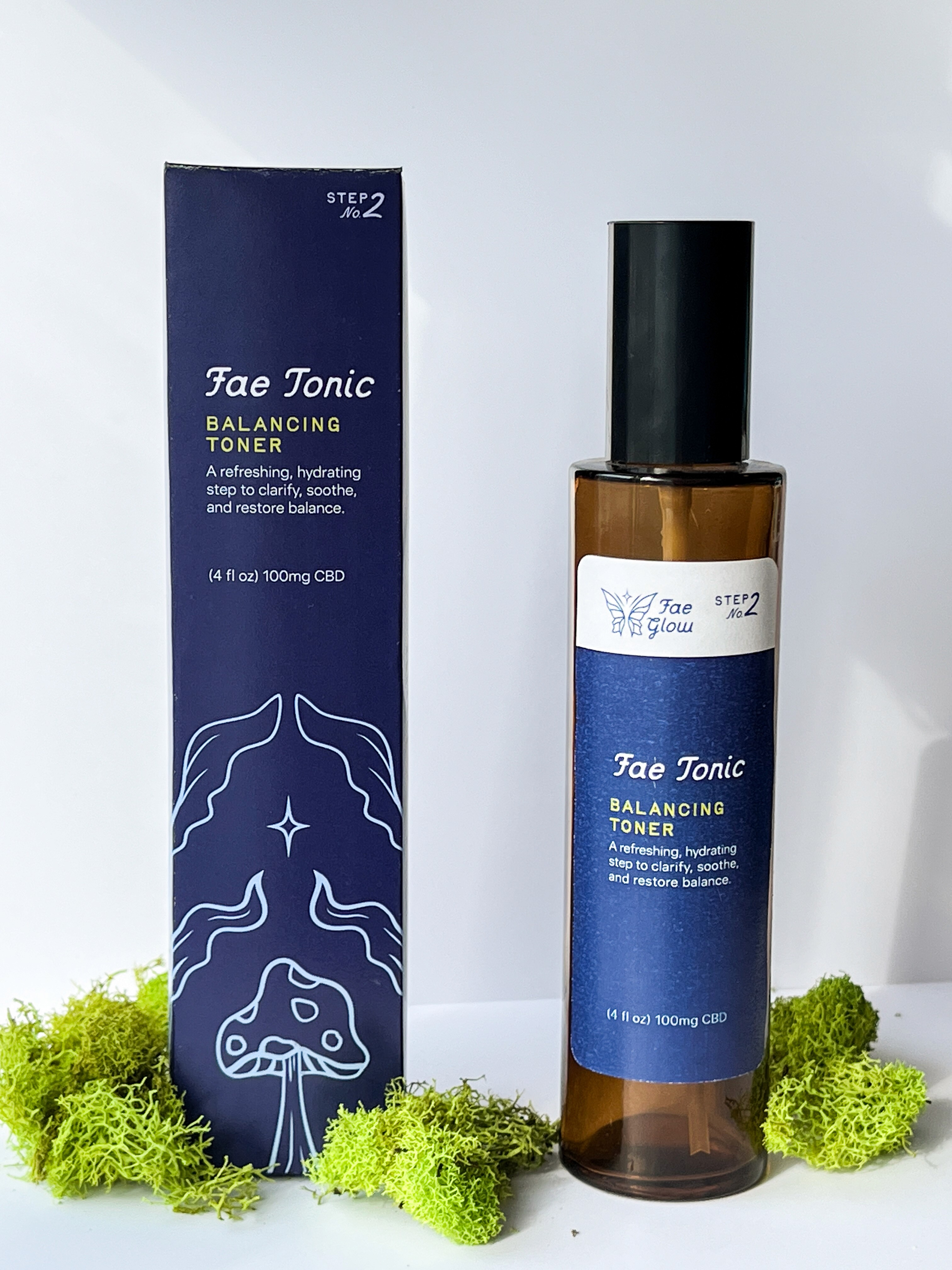A bottle of facial oil with a dark blue label and a matching box, surrounded by green leaves.