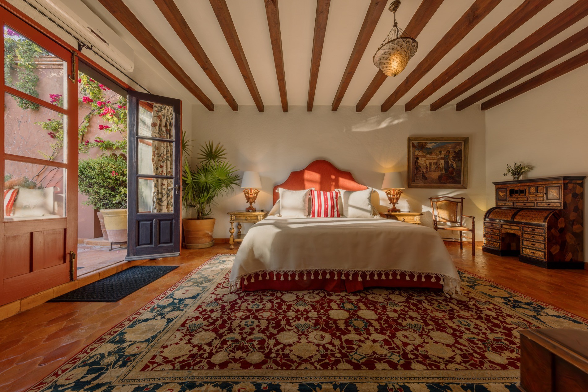 La Residencia guest bedroom with wooden beam ceiling, king bed, and French doors opening to courtyard