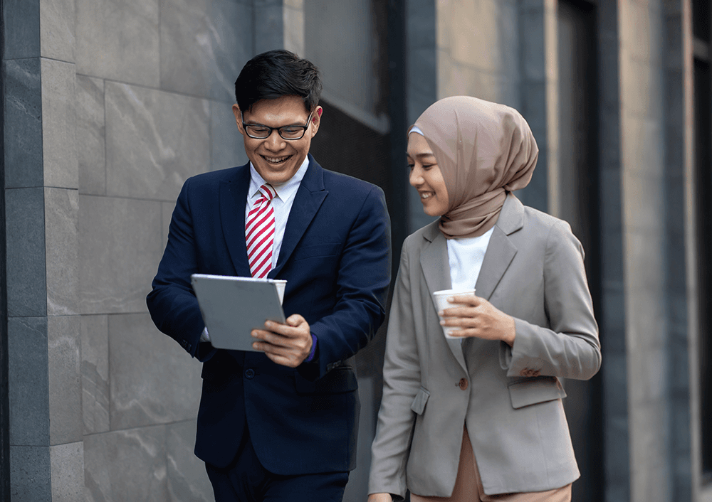 Asian couple in business attire, focused on a tablet in an office, driving efficiency and decision-making improvements together.