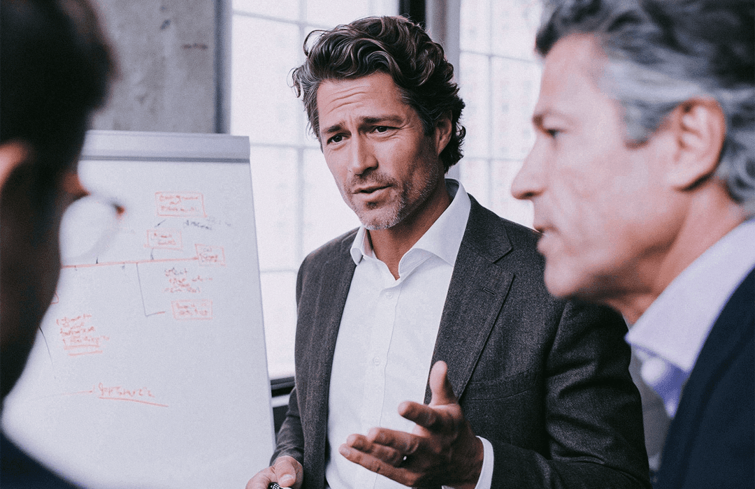 Homem de negócios gesticula explicando em reunião com flipchart, escritório luminoso. Blog post Inspira.