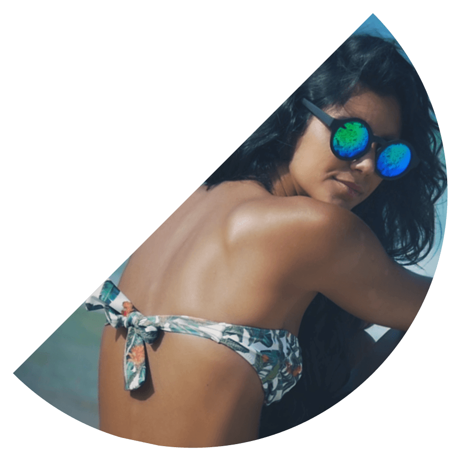 Editorial fashion film frame of a woman looking at the camera with sunglasses wearing a bikini at the beach