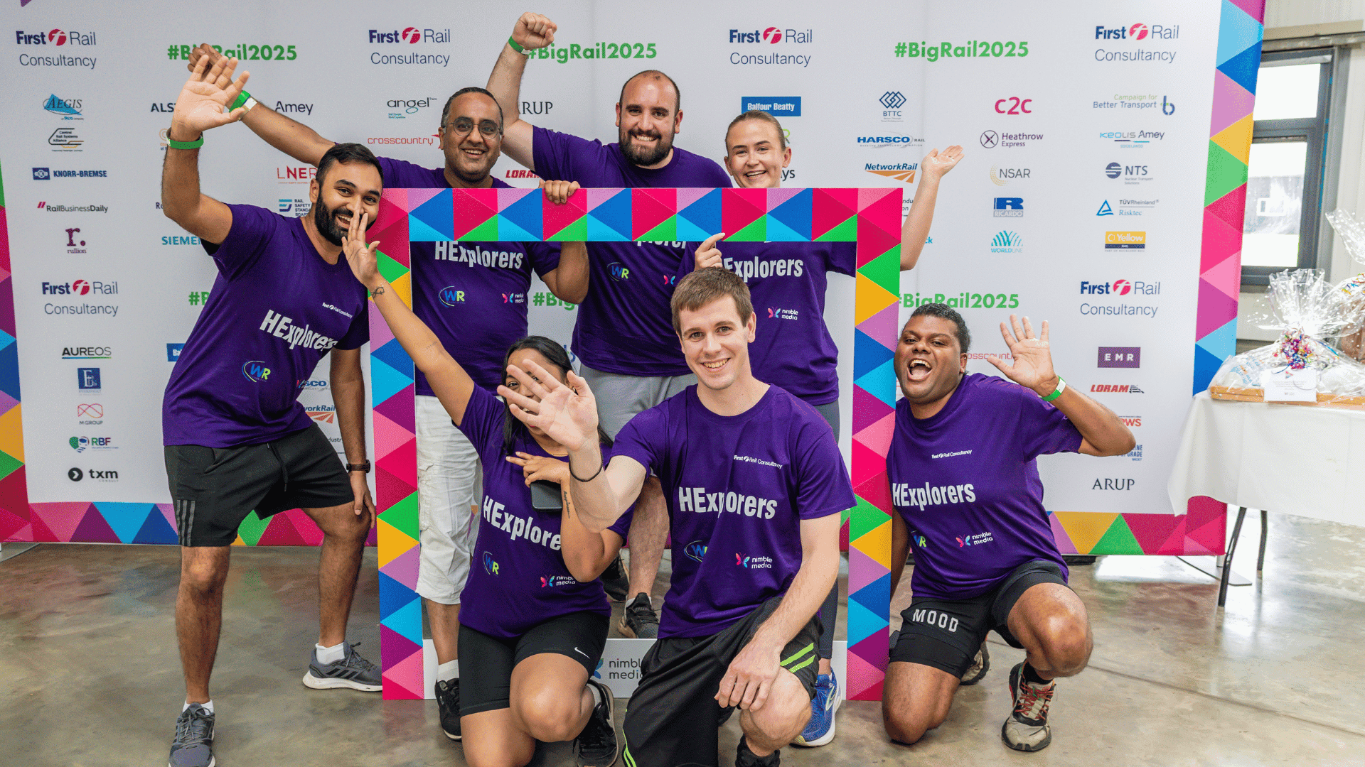 Outdoor team-building event with participants wearing matching blue shirts, taking part in inflatable obstacle courses and games, smiling and cheering, with the words 'ENTER A TEAM' in large bold white and green text across the image.