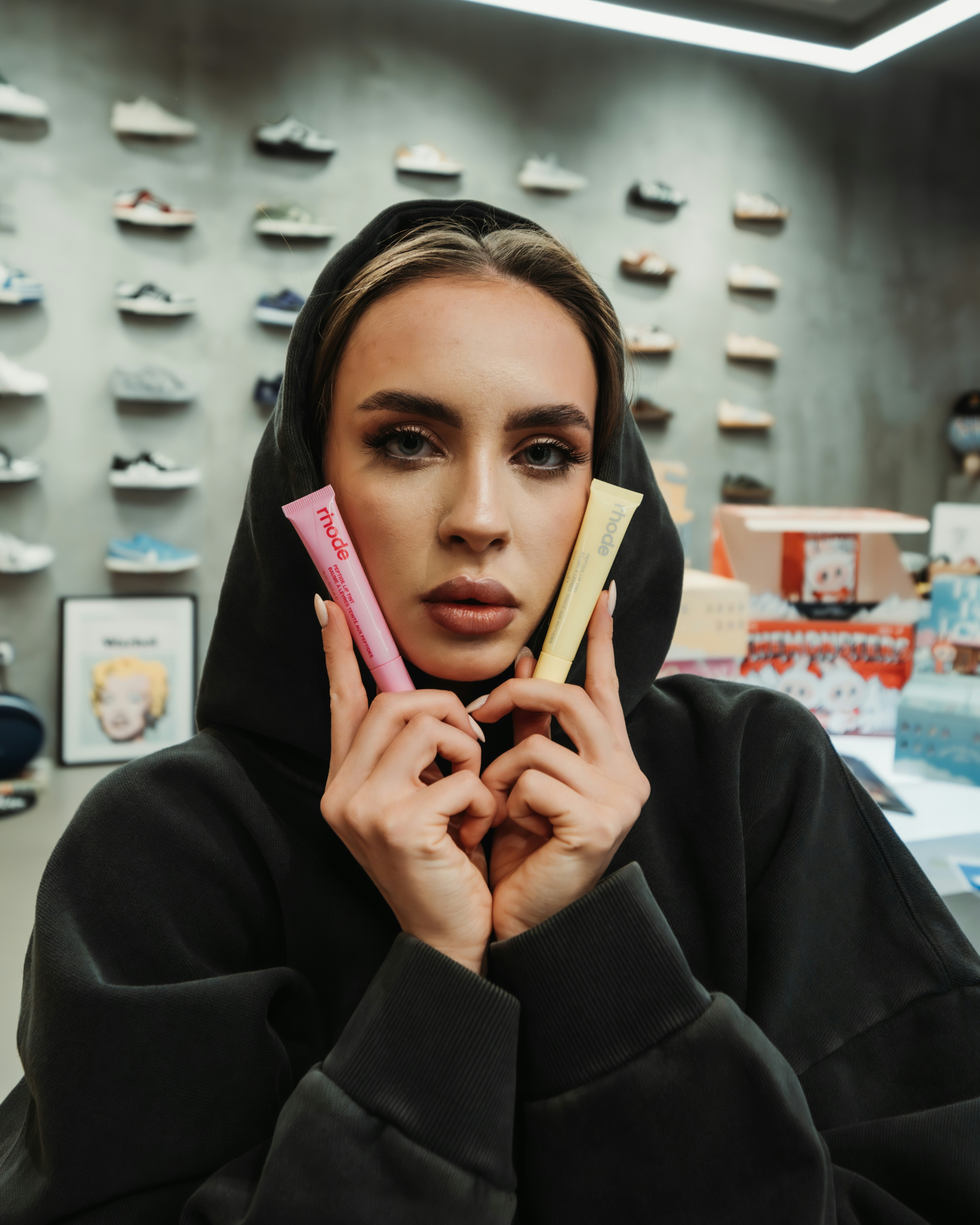 Woman in hoodie holds pink and yellow tubes