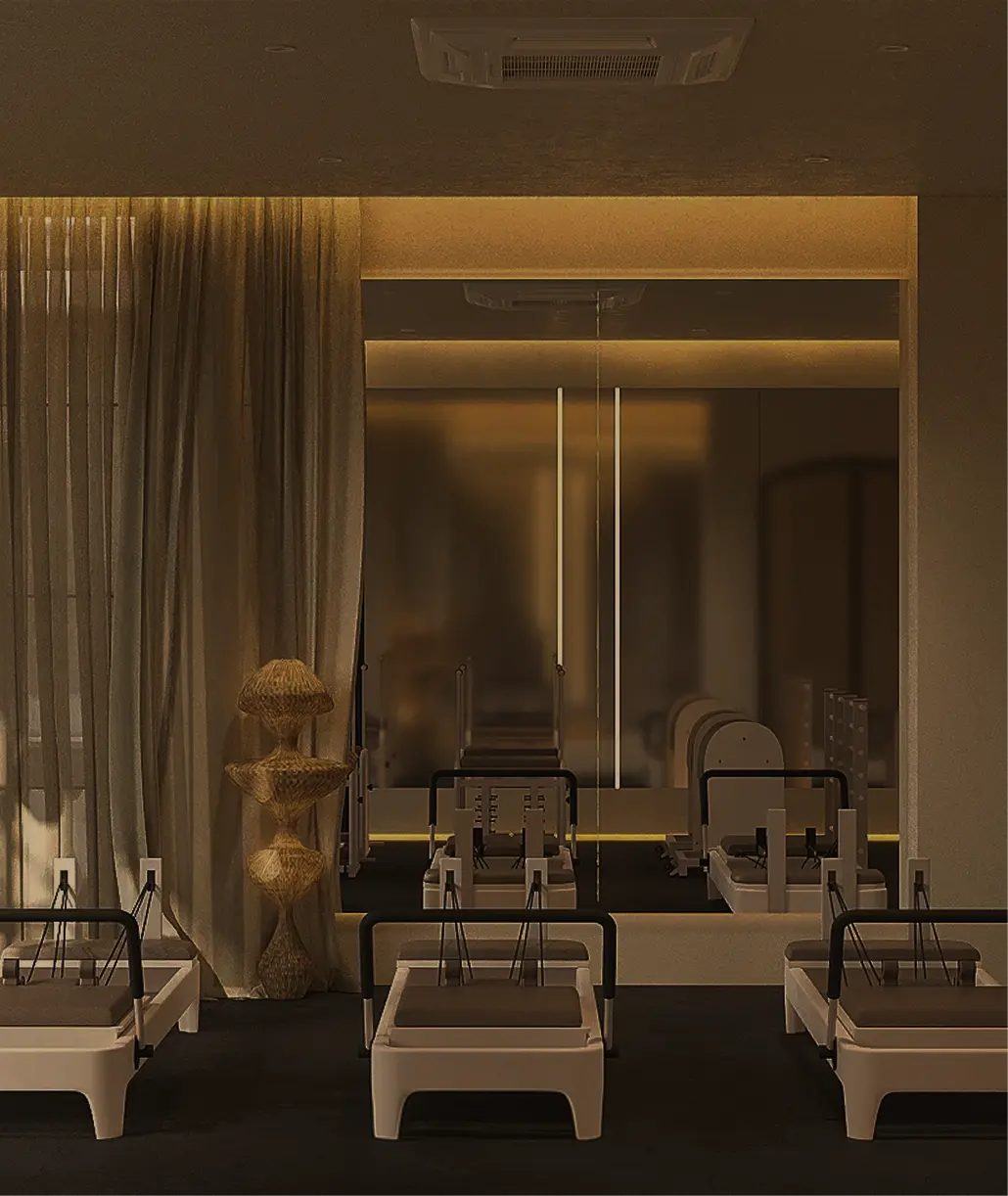 The image shows a dimly lit pilates studio featuring several reformer machines, sheer curtains, and mirrored walls creating a calming and modern atmosphere.