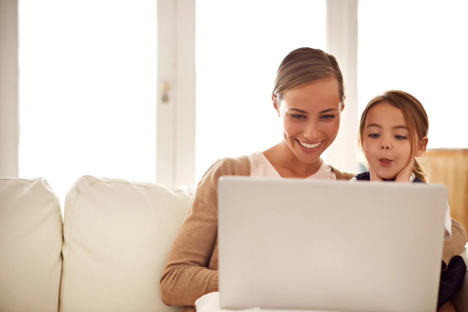 Mother and daughter smiling while using a laptop together on their couch