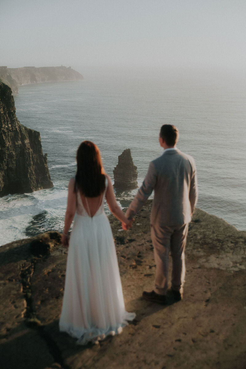 bride and groom holding hands with cliffs of moher in the background
