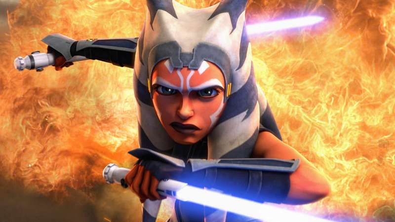 A front-facing Ahsoka holding two white lightsabers in front of a wall of fire. 