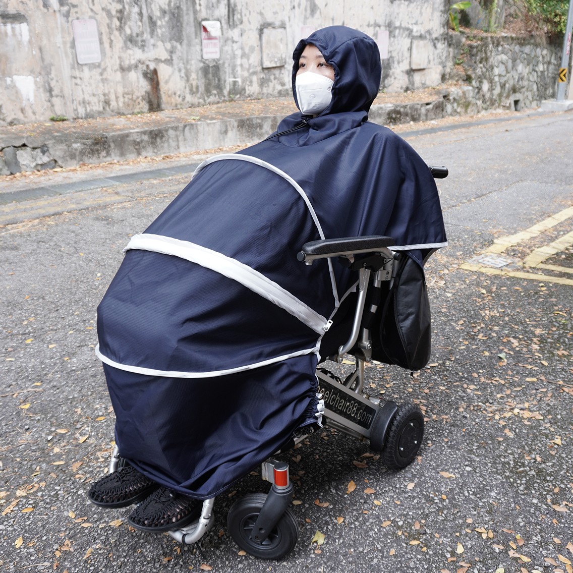 Final prototype of the wheelchair poncho in use outdoors by a wheelchair user, showing full-body coverage and adjustable neck and hem