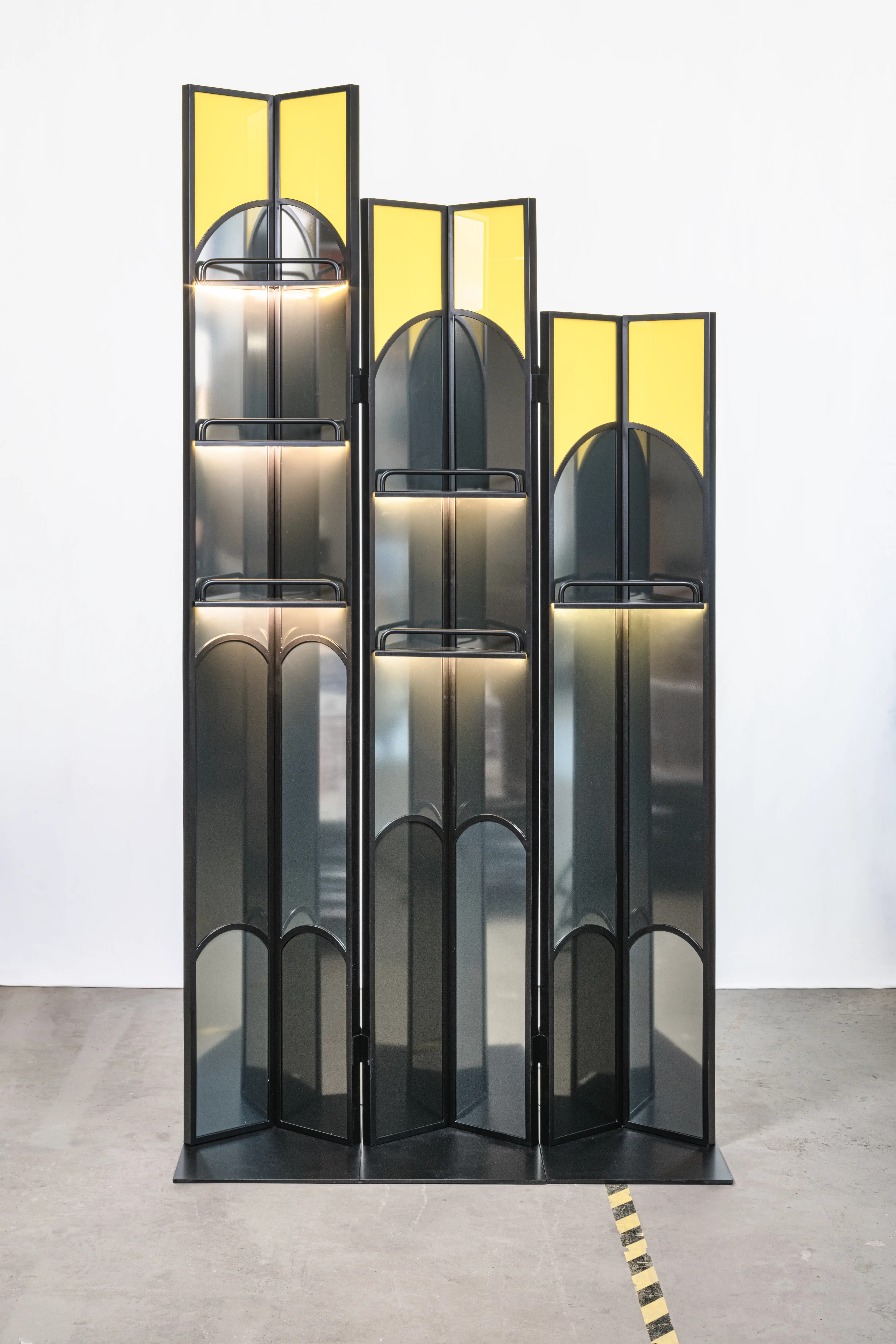 Three-part folding screen of the SCHWEPPES bartool set with black Art Deco arch frames, smoked glass panels, yellow accents and integrated illuminated shelves.