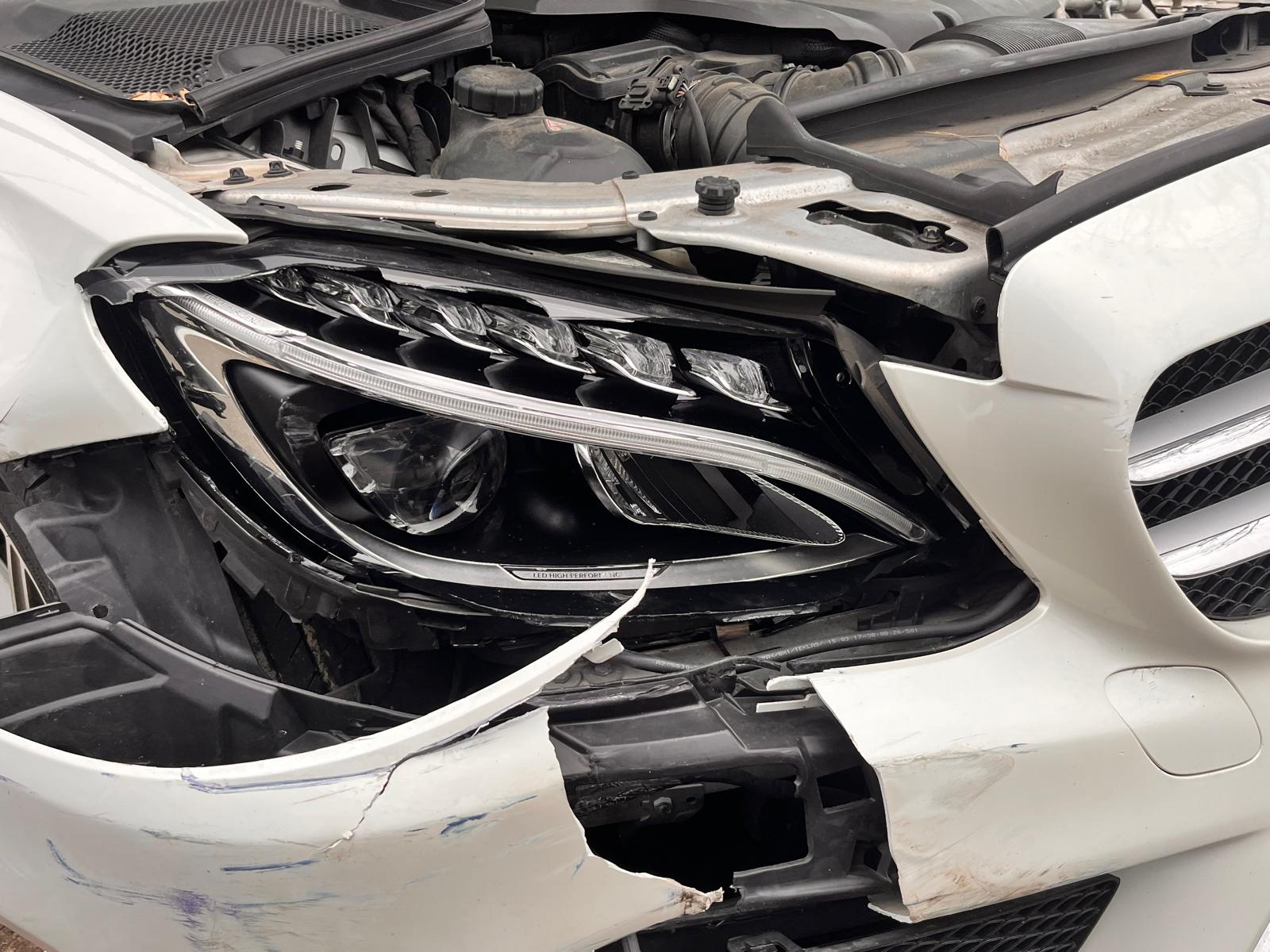 A professional car repair workshop showing a technician assessing accident damage on a vehicle while discussing repair options with the car owner. Documents and repair estimates are visible, illustrating the insurance claim process.