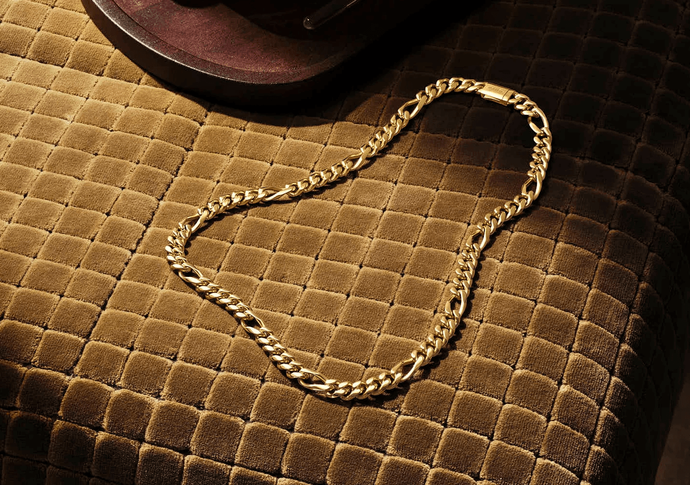 A simple gold chain laid on a textured brown surface, reflecting soft light.