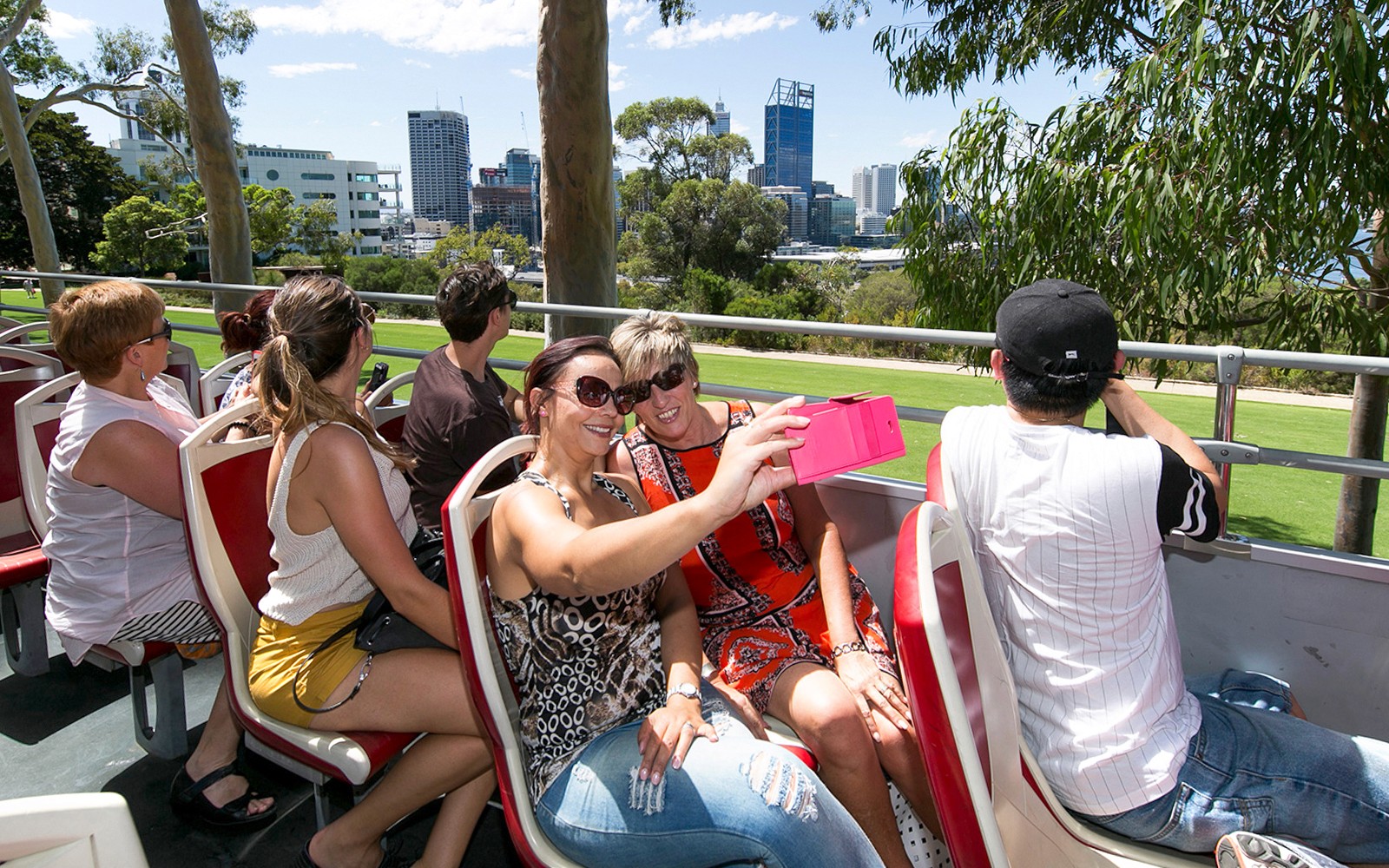 Tourists on a hop-on-hop-off bus in Kings Park, Perth, taking photos of the city skyline.
