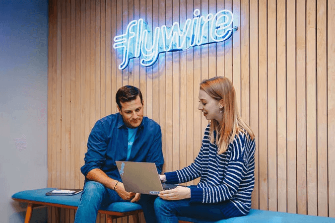 Two people sitting on a table, one using an open laptop.