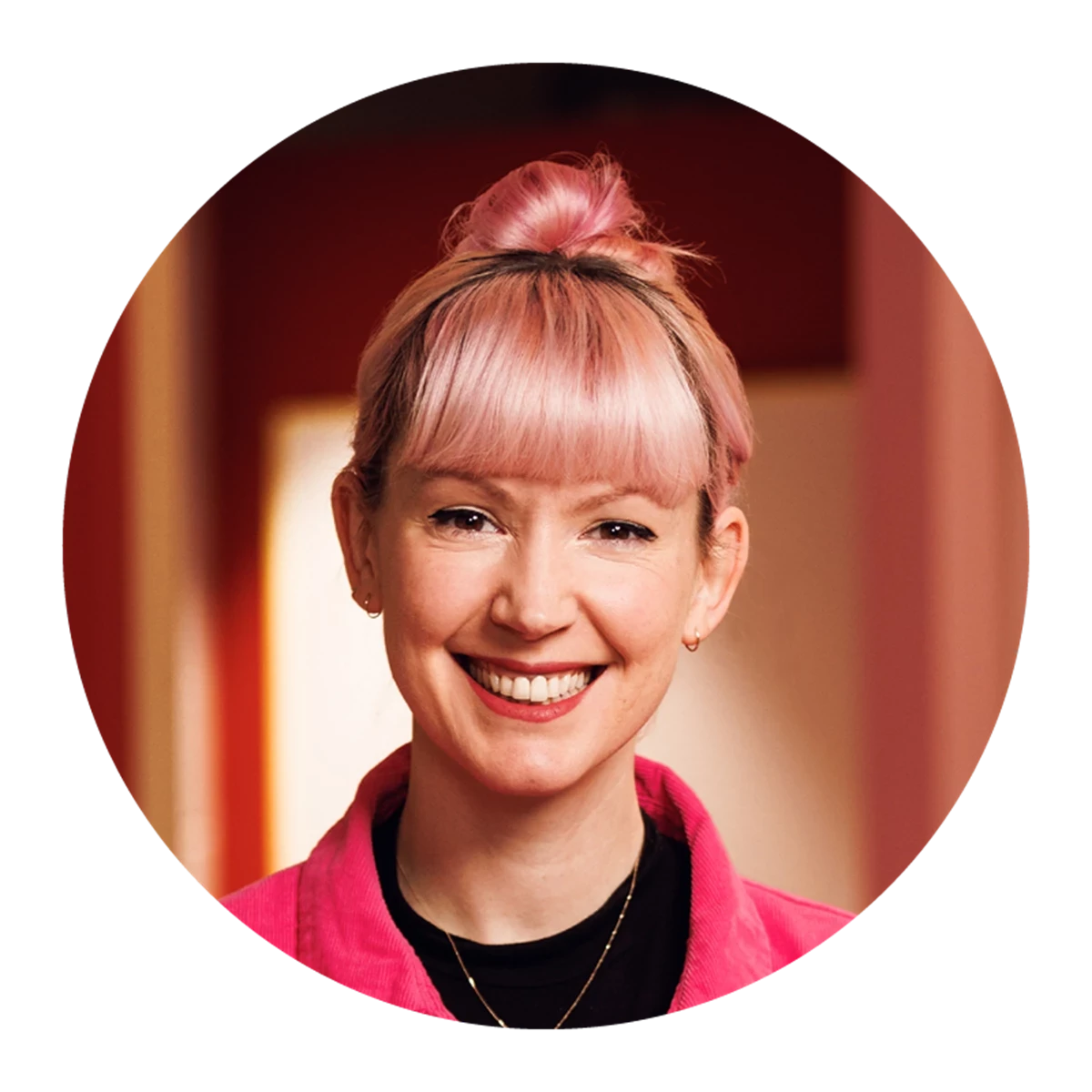 Person with pink hair in a top bun wearing a pink jacket and black top.