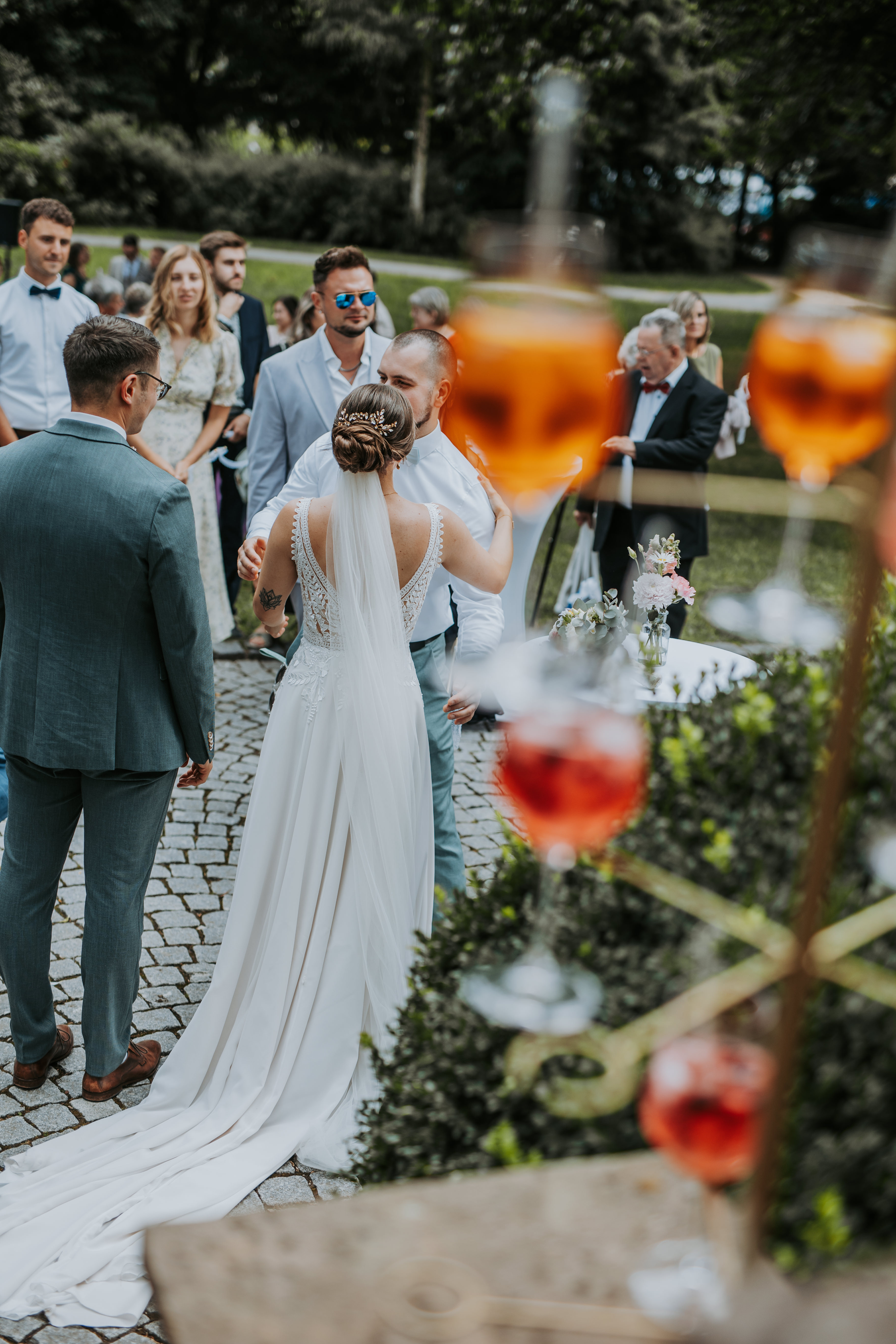 Brautpaar feiert mit Sektflaschen und Spritzern vor einem Gebäude.