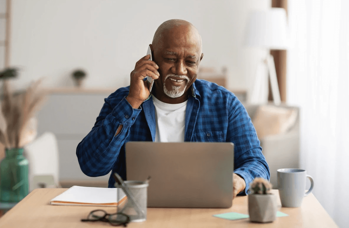 Senior man at computer, talking on smart phone