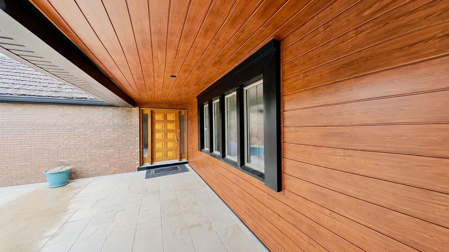 Galería y alero de una casa revestidos con metal siding símil madera tono roble, sobre paredes de ladrillo visto