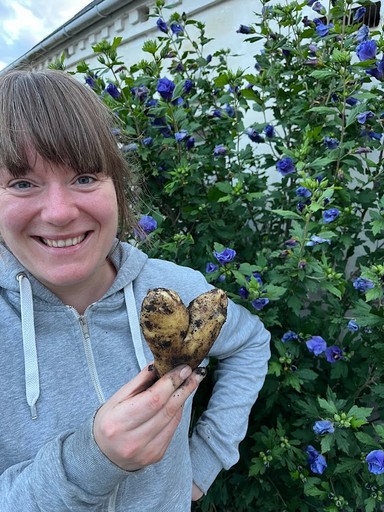 Anne står smilende med en hjertekartoffel fra den gravefrie køkkenhave hos Egebjerggård Grønt. 