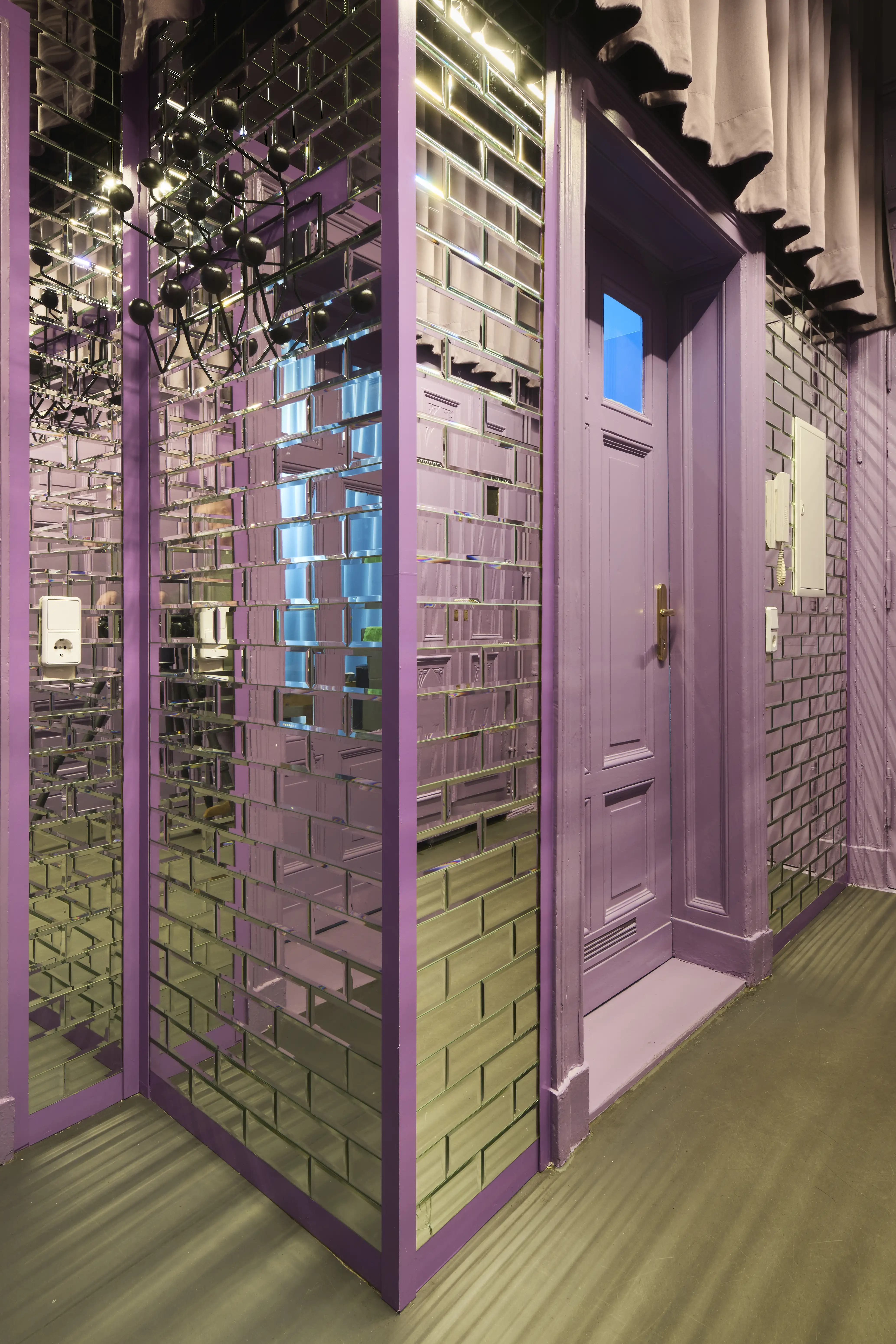 Hallway with mirror tile walls, lilac door frames and black ruffled curtain above.