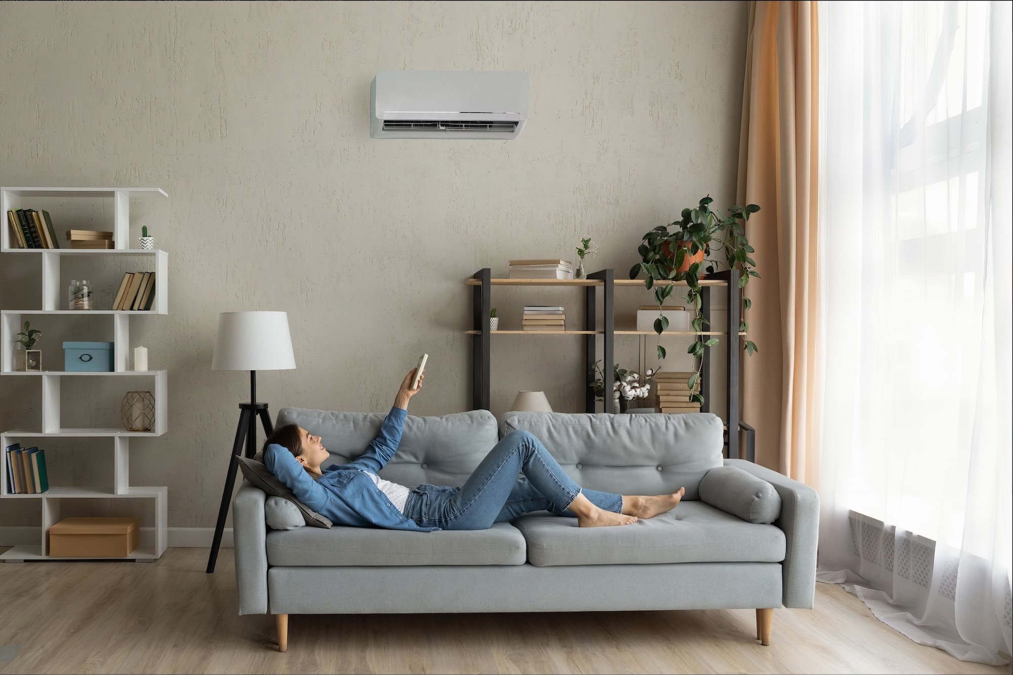 woman lying on sofa pointing remote at air conditioner