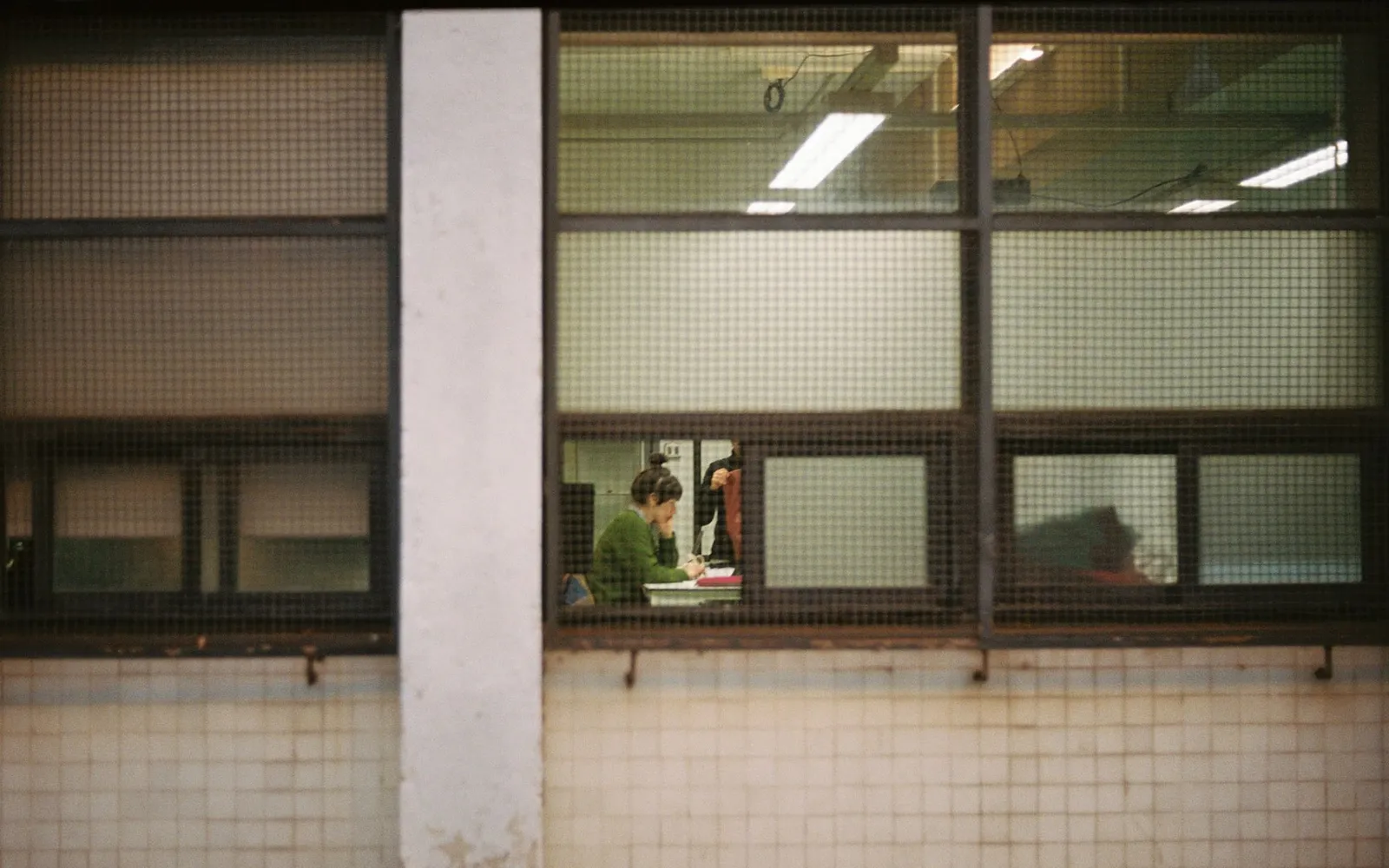 People working at desks, seen through the grid of a large industrial window