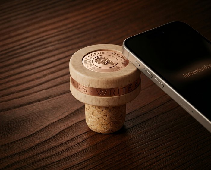 Wooden wine stopper with copper accents next to a smartphone on a wooden surface.