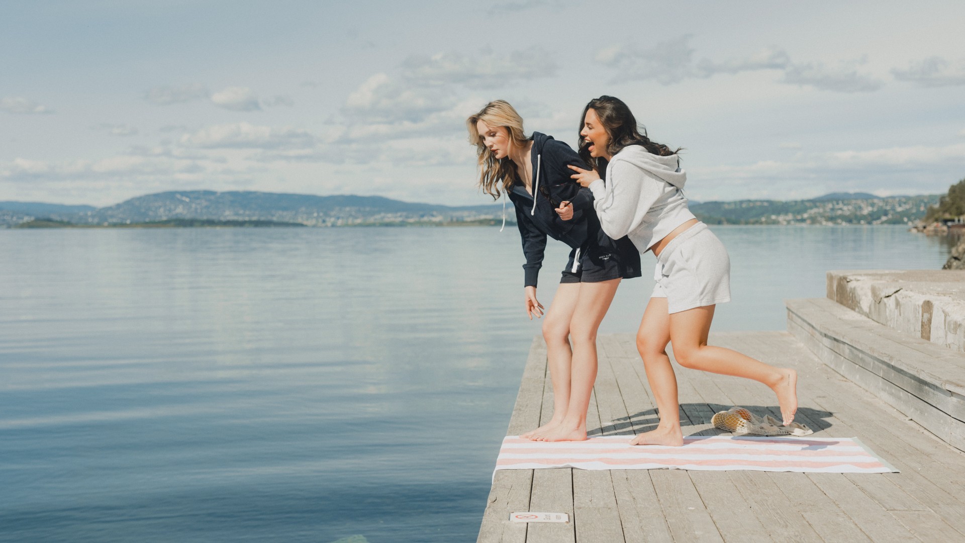 Two women by the water wearing navy and light grey hoodies with matching lounge shorts, relaxed casual summer outfits.