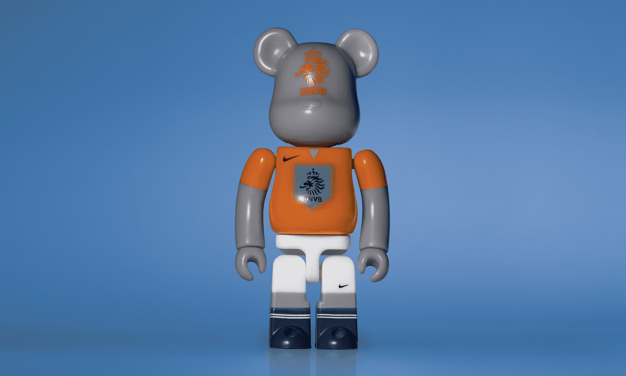 A single 3.5” tall Bre@rbrick/Nike toy created to commemorate the 2006 Holland World Cup football team. The toy is painted to appear in the Netherlands football kit and stands in the center of the frame in front of a blue background.