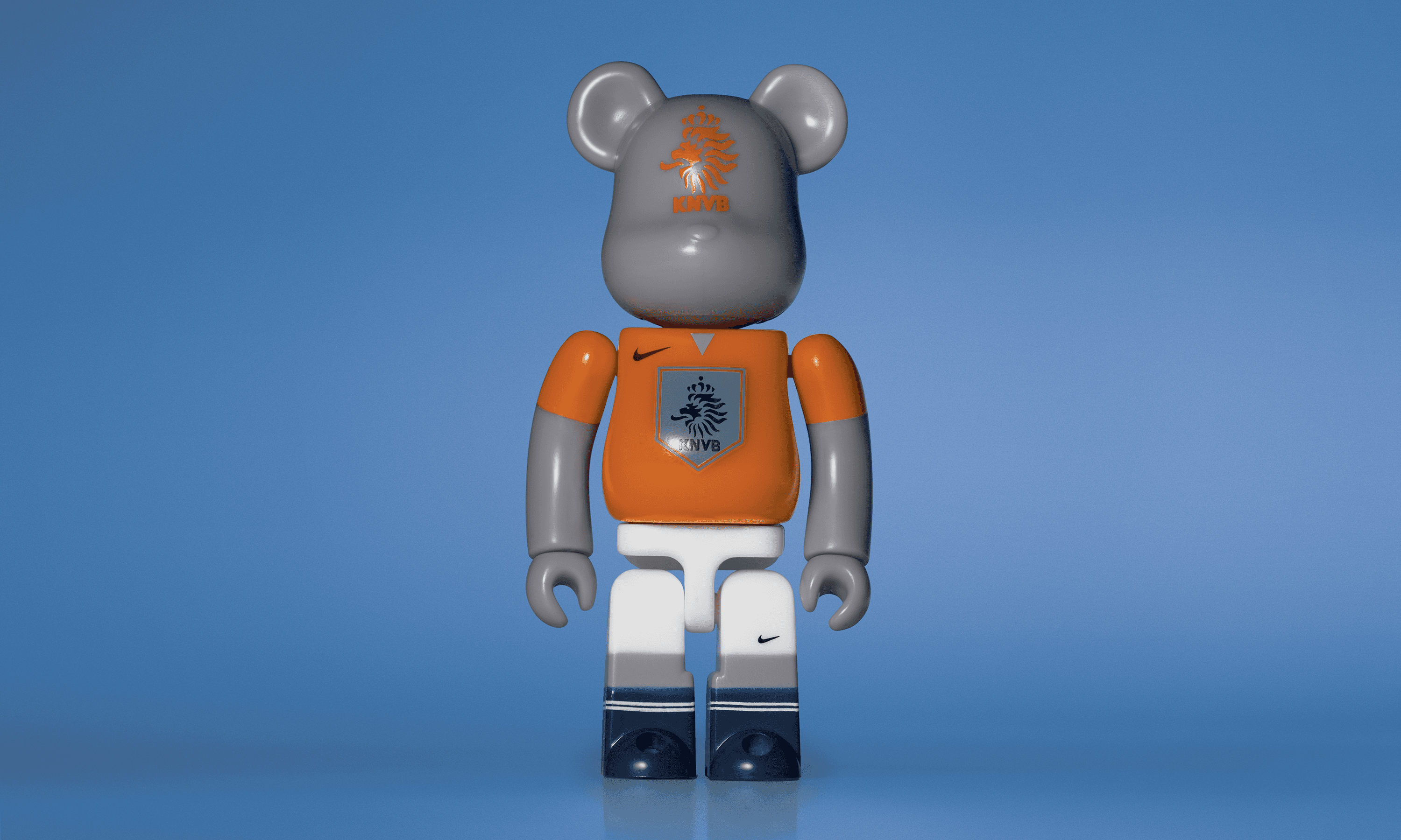A single 3.5” tall Bre@rbrick/Nike toy created to commemorate the 2006 Holland World Cup football team. The toy is painted to appear in the Netherlands football kit and stands in the center of the frame in front of a blue background. 