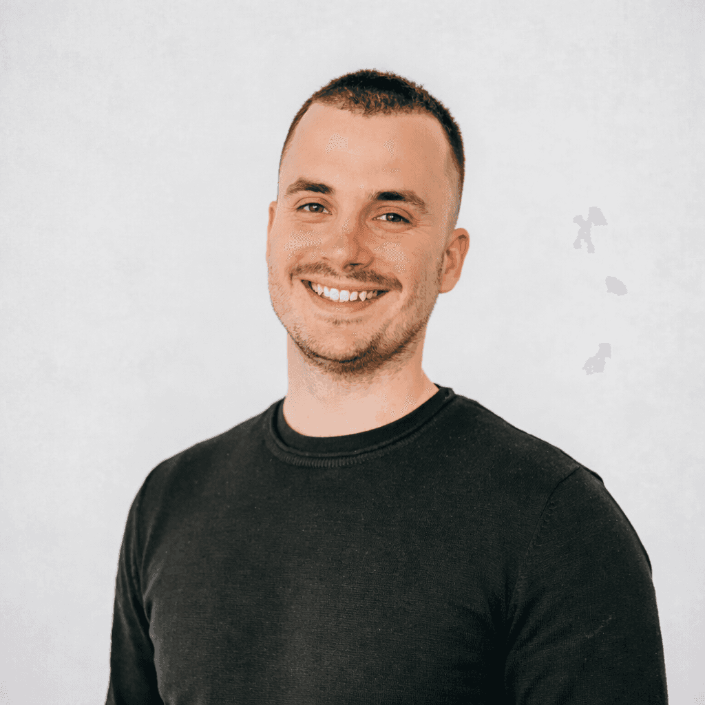 Minimal studio portrait of a confident woman in a white shirt, arms crossed, on a soft gray background.