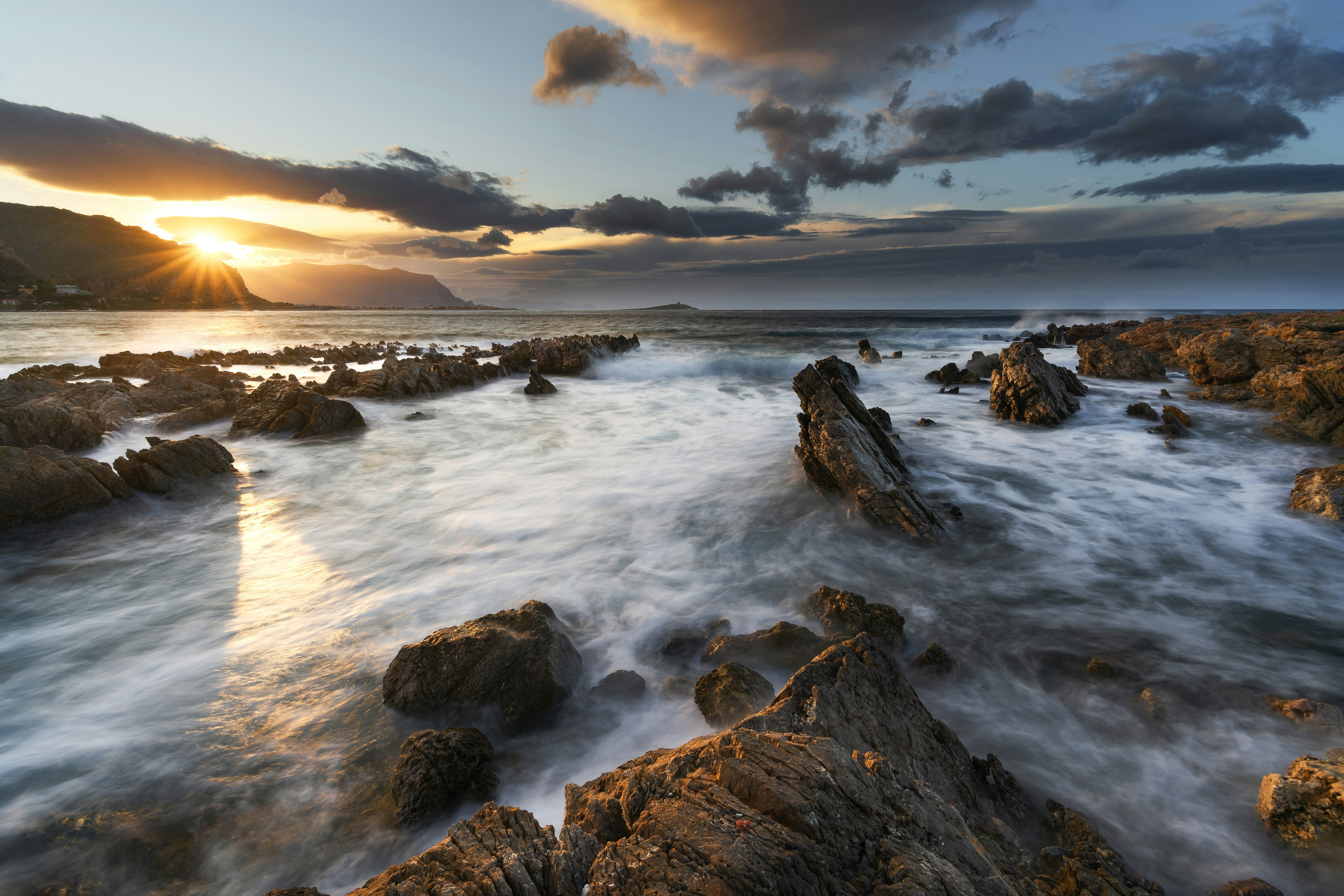 Rocky coastline with waves crashing at sunset.