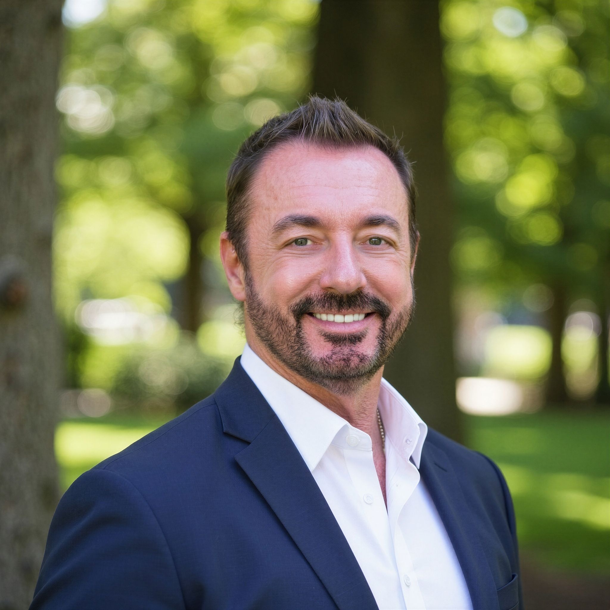 Smiling financial adviser in navy suit outdoors, surrounded by trees and greenery.