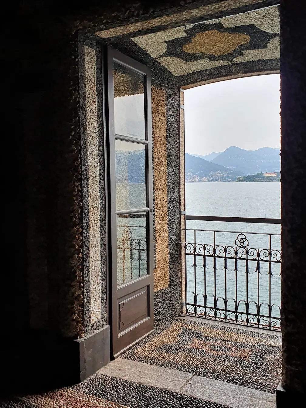 Tall french door opening onto a wrought-iron balcony overlooking a lake and mountains