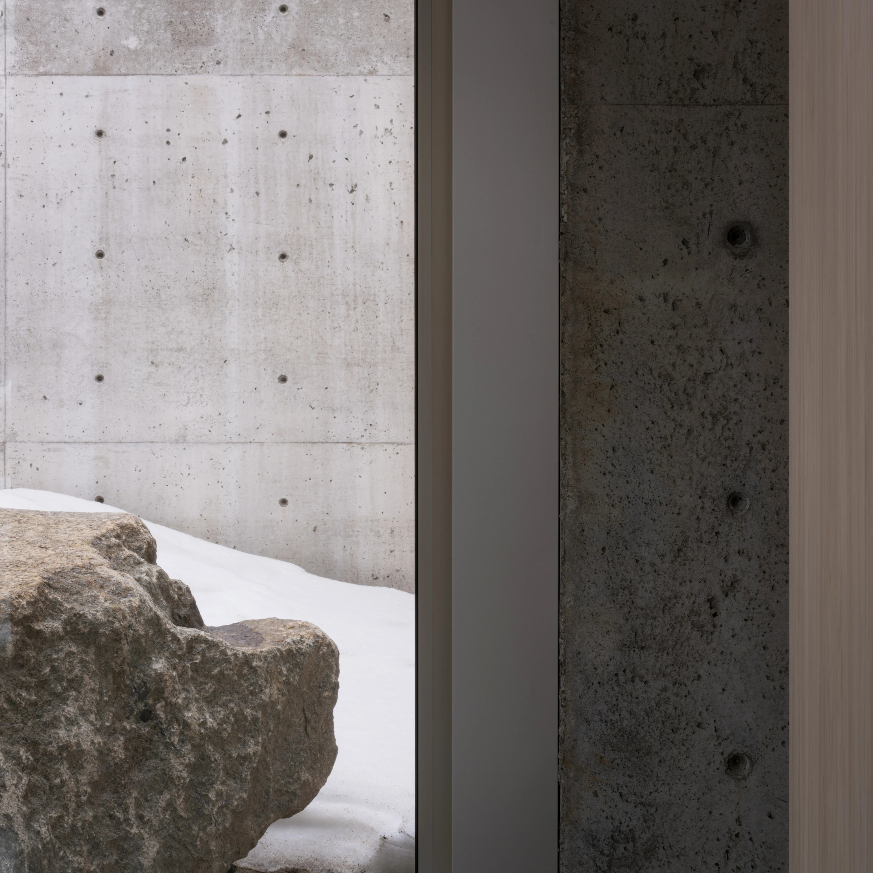 A minimalist interior featuring a concrete wall and a textured stone sculpture in a softly lit space.