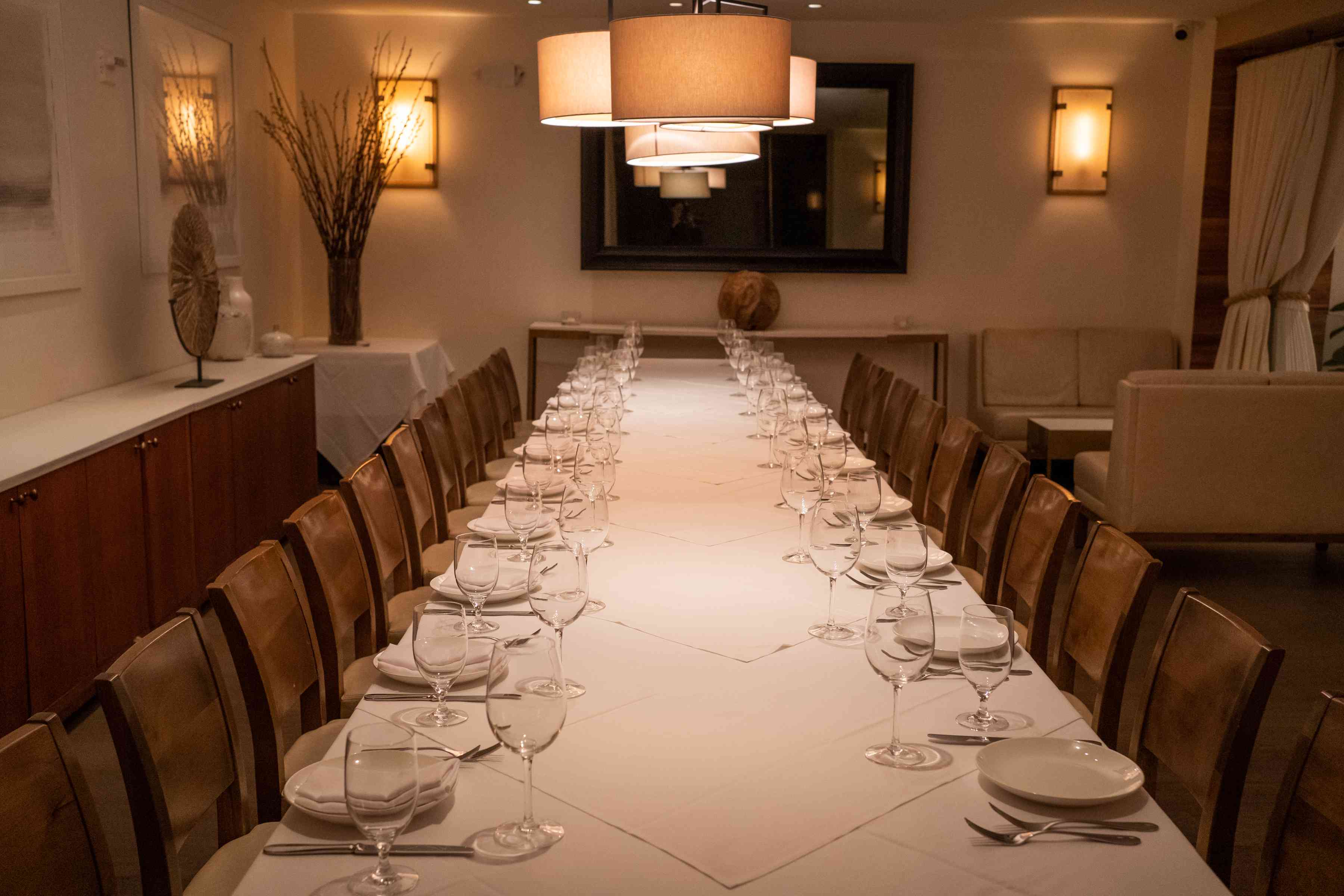 Long dining table set for a meal, with elegant lighting and a warm, inviting atmosphere.