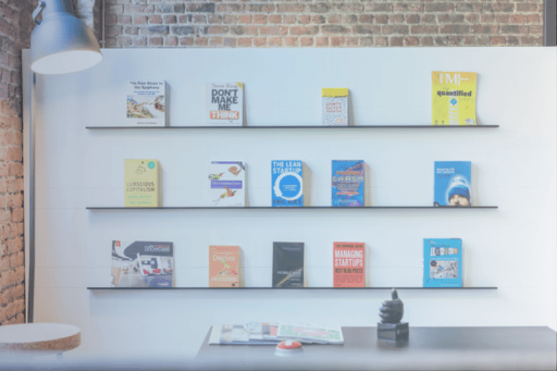 Shelves displaying best books on customer discovery and innovation in a stylish office with a brick wall backdrop.