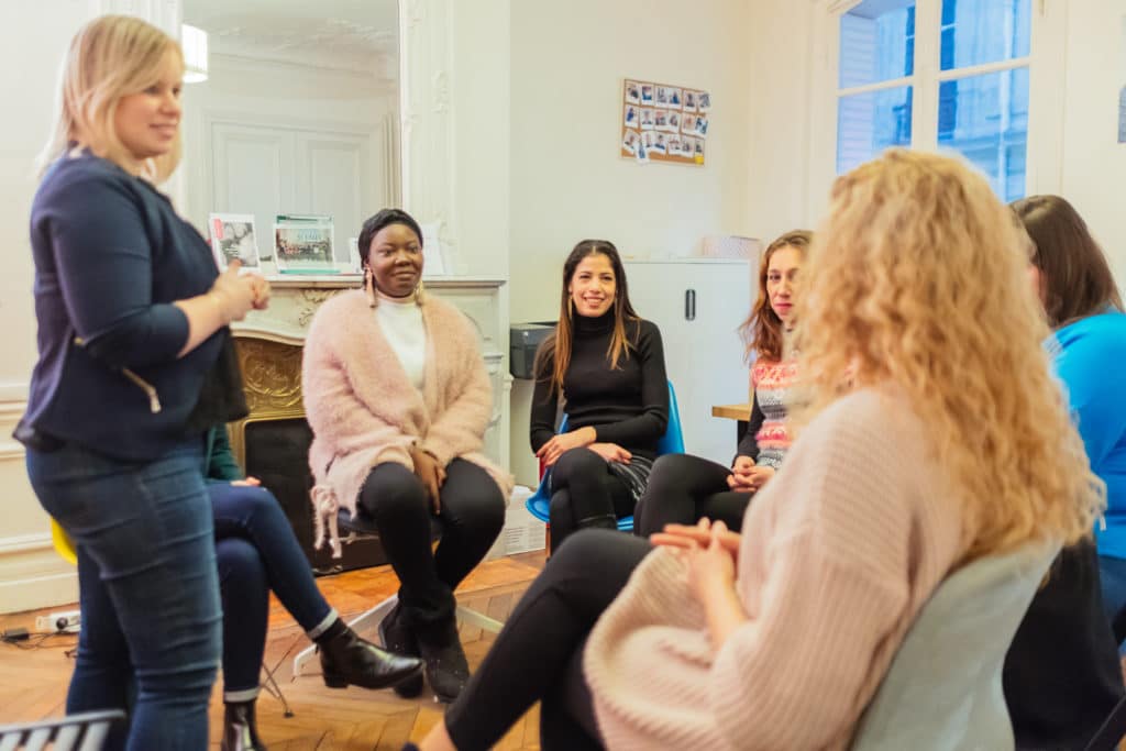 Une formatrice debout anime une session avec des auxiliaires de vie assises en cercle