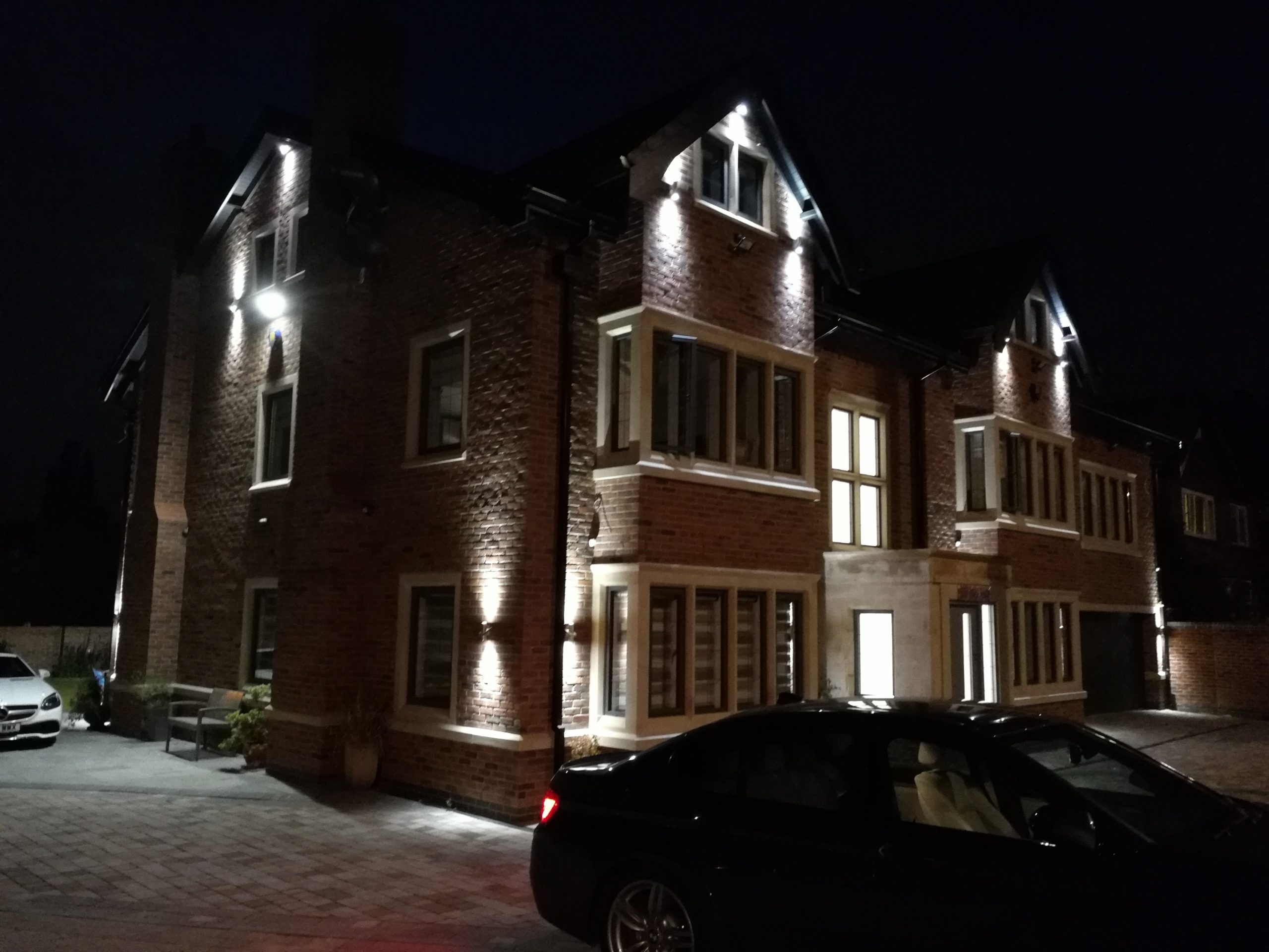 Night-time view of a luxury remodelled house with illuminated brickwork, stone detailing, and large feature windows.