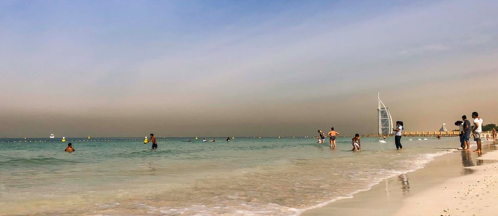 People enjoy Al Sufouh beach on cloudy day: relaxing, various beach activities.