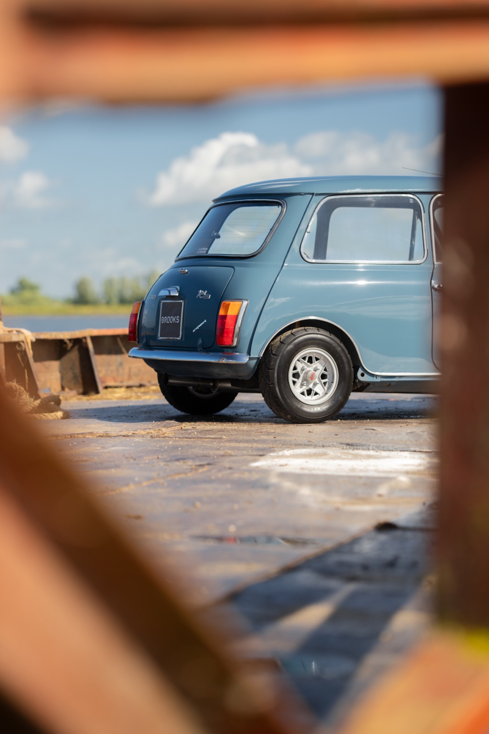 A blue vintage car parked outdoors, framed by wood, with a clear blue sky in the background.