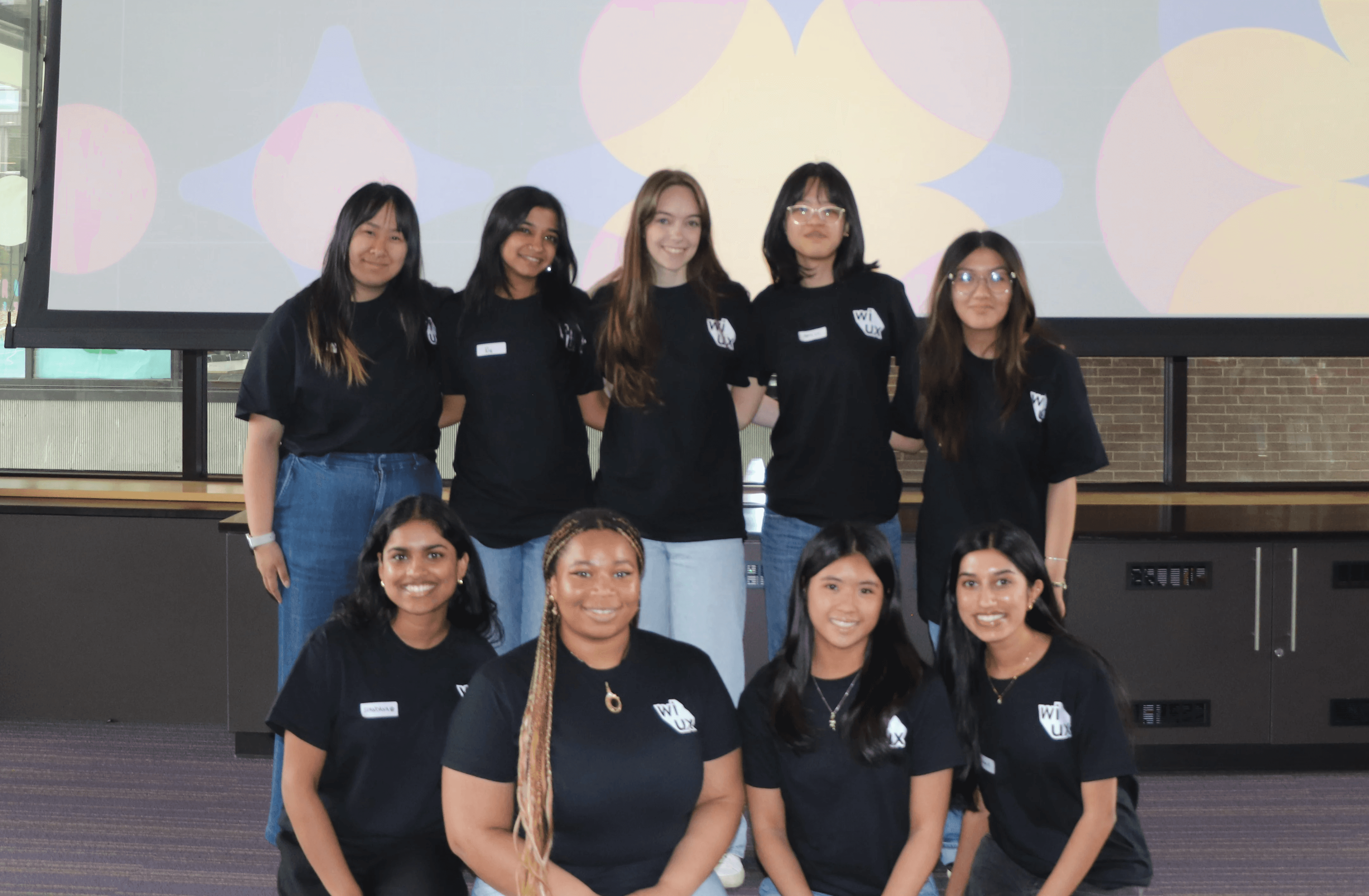 The Women in UX team at their 11th annual conference, standing in front of a projector.