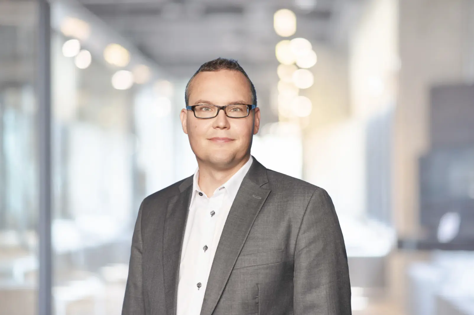 Dr. Johannes Rückert, Vorstand KWA Kuratorium Wohnen im Alter gAG, Portrait eines Mannes mit Brille im grauen Anzug vor unscharfem Bürohintergrund.