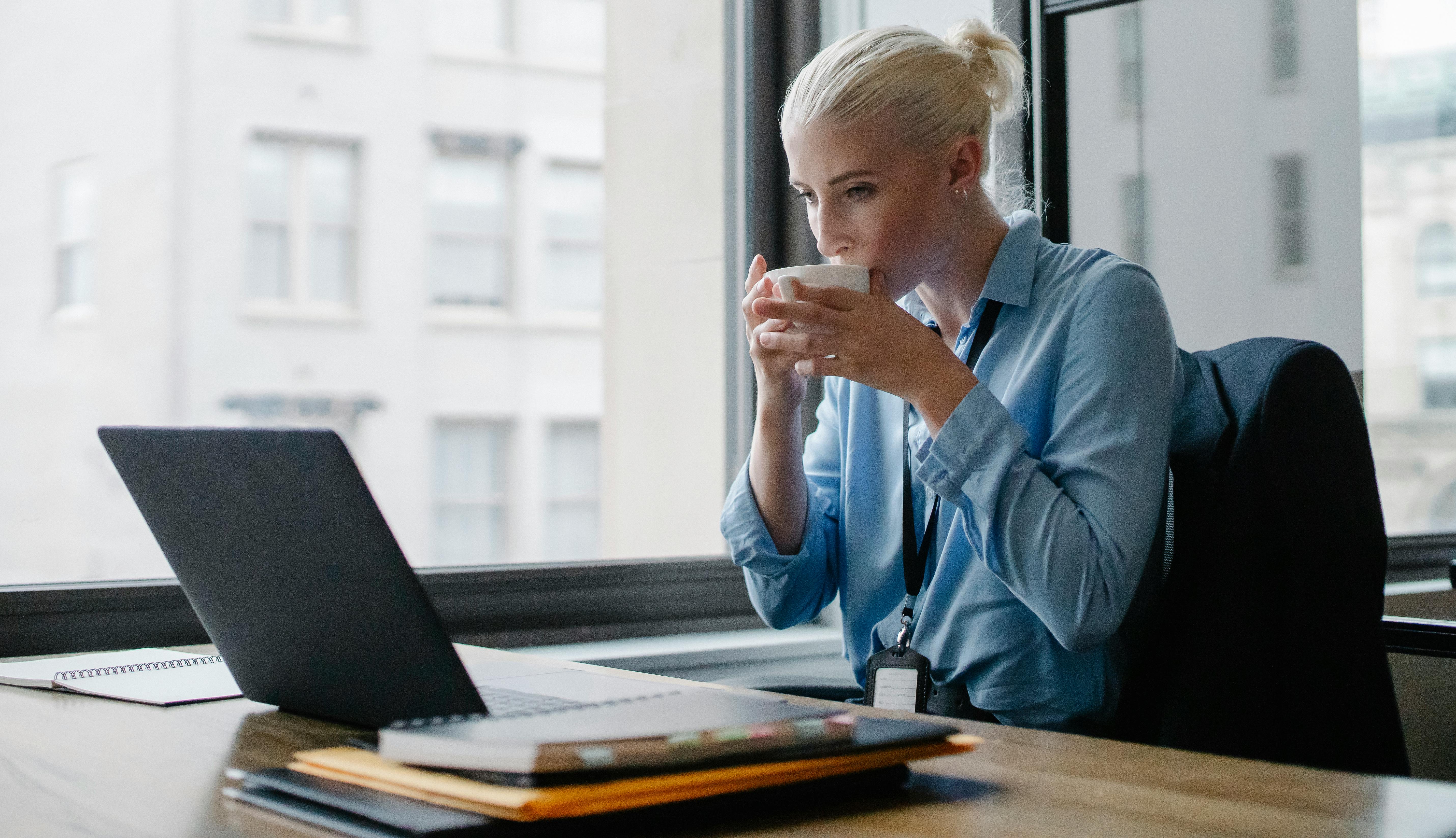 Woman drinking coffee while reading cold emails at workspcae