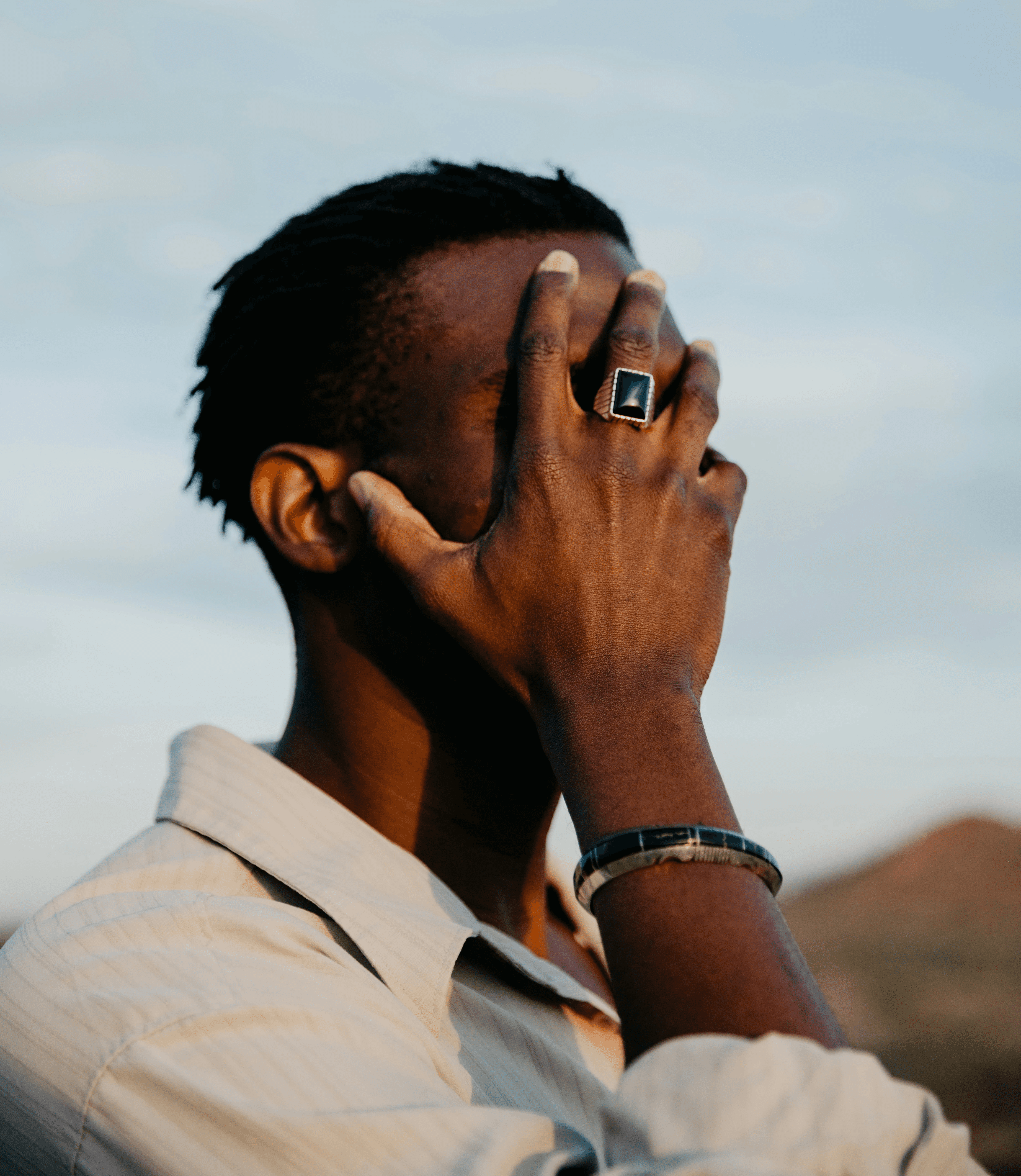 Man covering face with hand, wearing a ring.