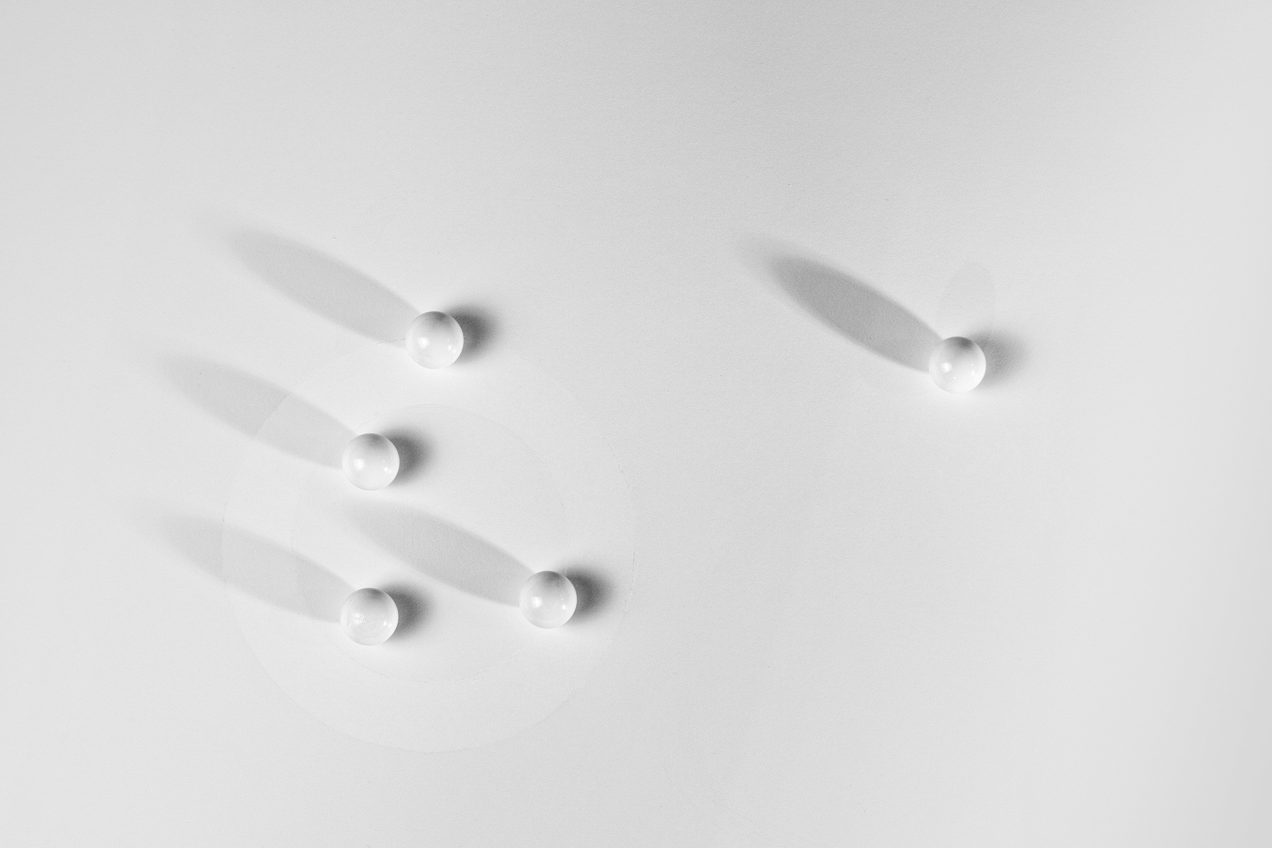 Photograph of five white marbles arranged loosely on a white surface with long cast shadows.