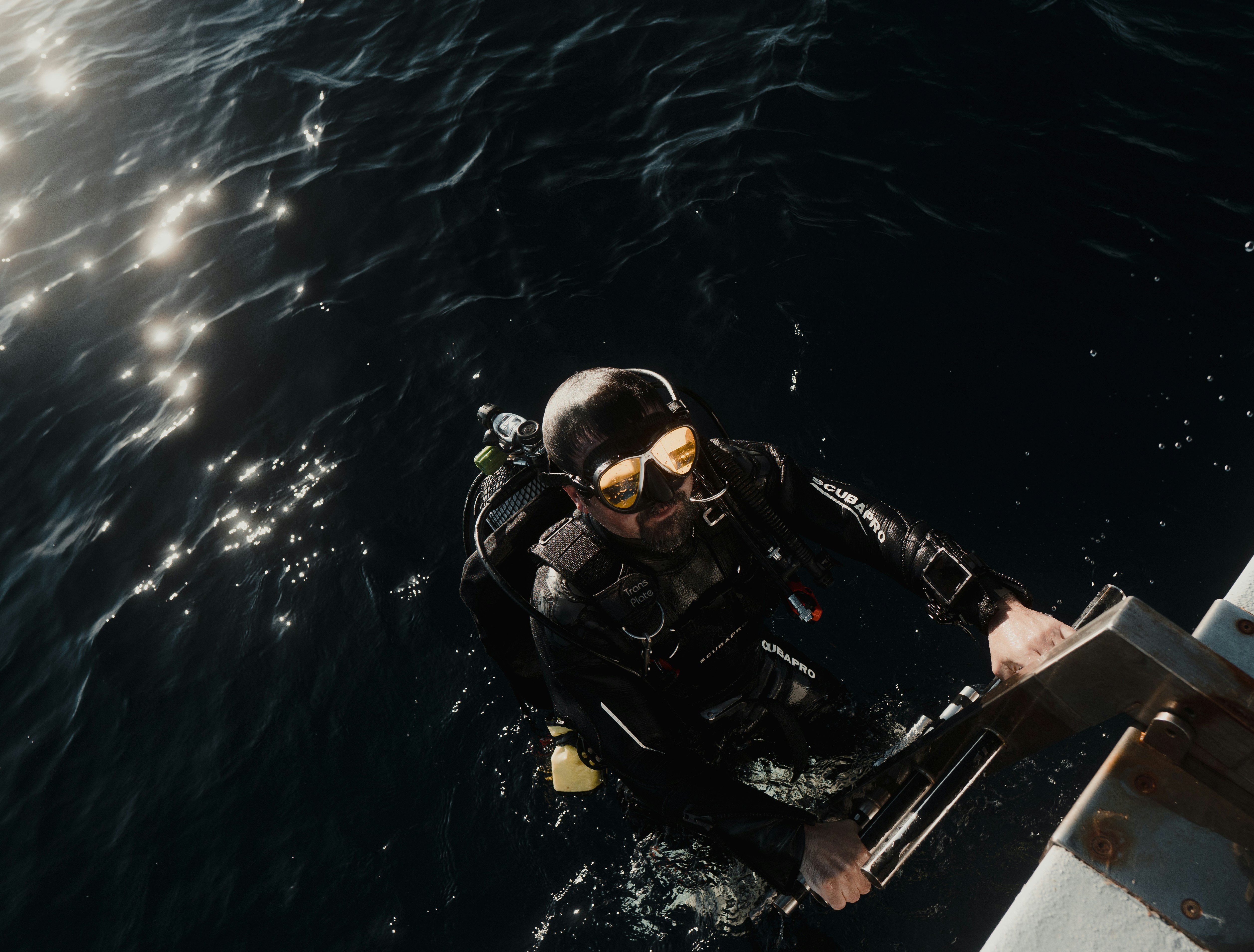 Scuba diver in full gear climbing a boat ladder before an underwater hull cleaning service.