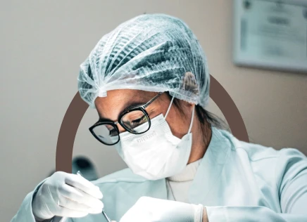 Dentista Nathália Dias em clínica odontológica usando máscara, touca e luvas durante procedimento dental, transmitindo segurança, higiene e atendimento profissional.
