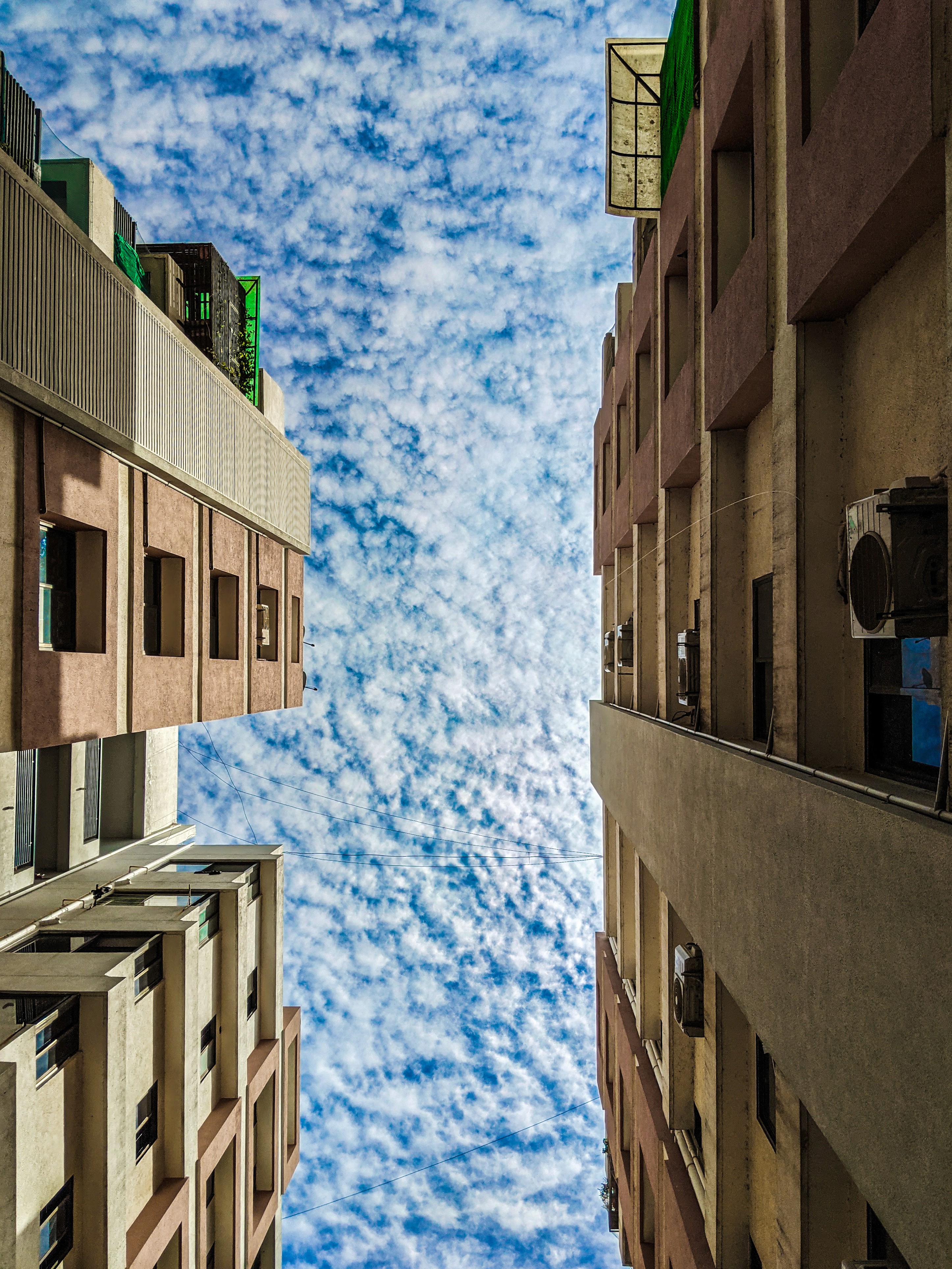 Architectural photography looking up between tall buildings, showcasing symmetry and form by Samuel Singh Bhakuni.
